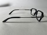 pair of black glasses on a white surface with a pen in the background