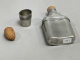 silver flask with a walnut and a shot glass on a white table