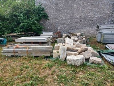 a pile of wood sitting in the grass next to a brick wall