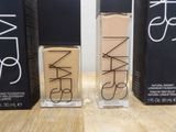 two bottles of nars cosmetics sitting on top of a wooden table
