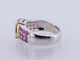 a close up of a ring with pink and yellow stones on a white surface