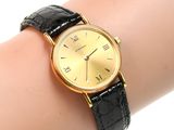 an image of a woman ' s wrist with a gold watch on it