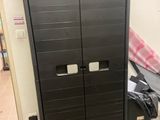 une armoire noire à deux portes et un sac noir posé par terre
