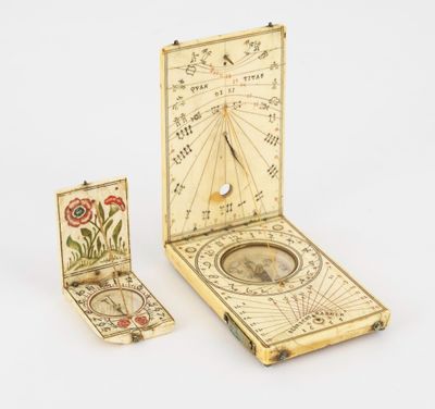 un cadran solaire ancien, accompagné d'une boussole et d'un livre, posé sur une surface blanche