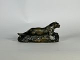 statue en bronze représentant un chien allongé sur un rocher, sur fond blanc