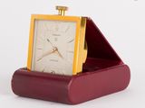 une petite horloge posée dans un écrin rouge sur une surface blanche