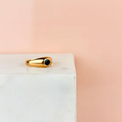 a gold ring with a black stone sits on top of a marble block