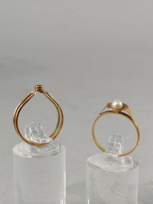 two gold rings with a pearl on top of a clear glass stand