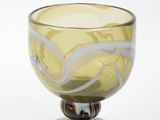 un bol en verre jaune posé sur un socle en bois, sur fond blanc