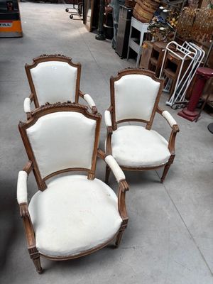 trois chaises blanches posées sur un sol en béton, à côté d'un tas de bric-à-brac