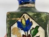a hand holding a small vase with flowers painted on it