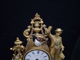 a gold clock with a man and a woman on it