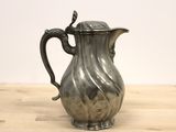 a silver pitcher on a wooden table with a white wall in the background