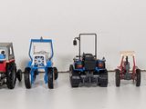 many toy tractors lined up in a row on a white surface