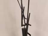 tall black metal tree sculpture on a pedestal with a white background