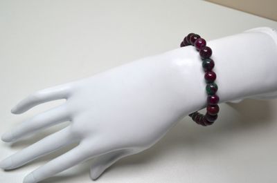 une main de mannequin blanche ornée d'un bracelet de perles rouges