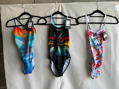 three swimsuits hanging on a clothes hanger on a wall