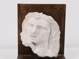 une sculpture blanche représentant le visage d'une femme, posée sur un socle en bois