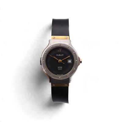 une image représentant une montre-bracelet noire et dorée posée sur une surface blanche