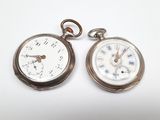 deux montres de poche en argent posées l'une à côté de l'autre sur une surface blanche