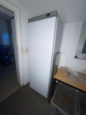 un réfrigérateur blanc dans un coin d'une pièce où se trouve une poubelle