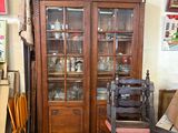 a wooden cabinet with a glass door and a chair in front of it