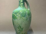 a green vase sitting on a table next to a white wall
