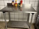 une table en acier inoxydable dans une cuisine, sur laquelle sont disposées des épices