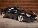 a picture of a black sports car parked in front of a brick wall