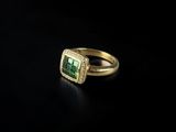a close up of a ring with a green stone surrounded by diamonds