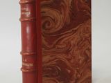 an old book with a red cover sitting on top of a white table