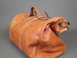 brown leather duffel bag with zippers and handles on grey background