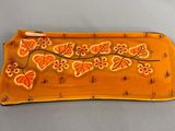 une assiette jaune ornée de fleurs et de feuilles orange, posée sur une table