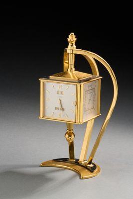 une image représentant une horloge dorée posée sur un socle, sur une surface grise