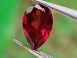 un gros plan sur un diamant rouge en forme de cœur tenu par une paire de pinces