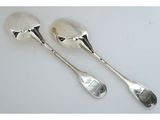 deux cuillères en argent et un repose-cuillère posés sur une surface blanche