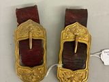 une paire de boucles anciennes en laiton avec des lanières en cuir rouge