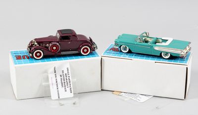 Deux petites voitures sont posées dans une boîte sur une surface blanche.