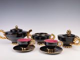 three black and gold tea cups and saucers on a white table