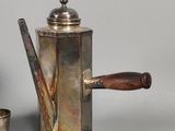 a silver coffee pot with a wooden handle next to a silver cup