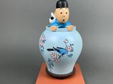vase bleu et blanc sur lequel est assis un homme, avec un oiseau perché au sommet du vase