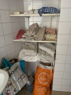 une salle de bains carrelée de blanc, avec un lavabo blanc et des étagères