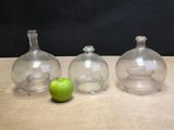 three glass vases sitting next to an apple on a table
