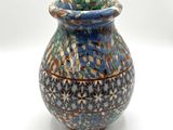 un vase bleu et brun posé sur une surface blanche