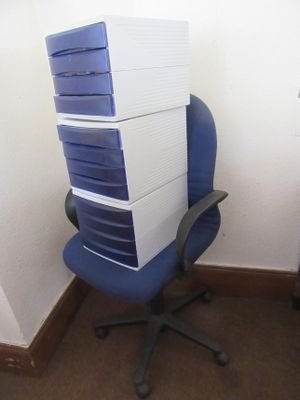 des cartons empilés sur une chaise de bureau bleue, dans un coin