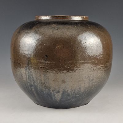 un vase brun et noir posé sur une surface blanche