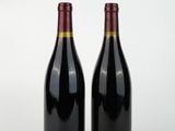 two bottles of red wine sitting next to each other on a white surface