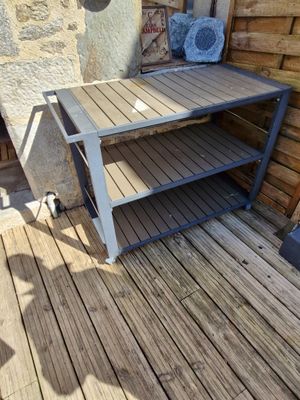 une table en bois posée sur une terrasse en bois, près d'un mur en pierre