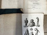 Quelqu'un tient un livre ouvert posé sur un plancher en bois sur lequel figurent des dessins.