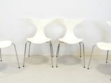 quatre chaises blanches alignées contre un mur blanc